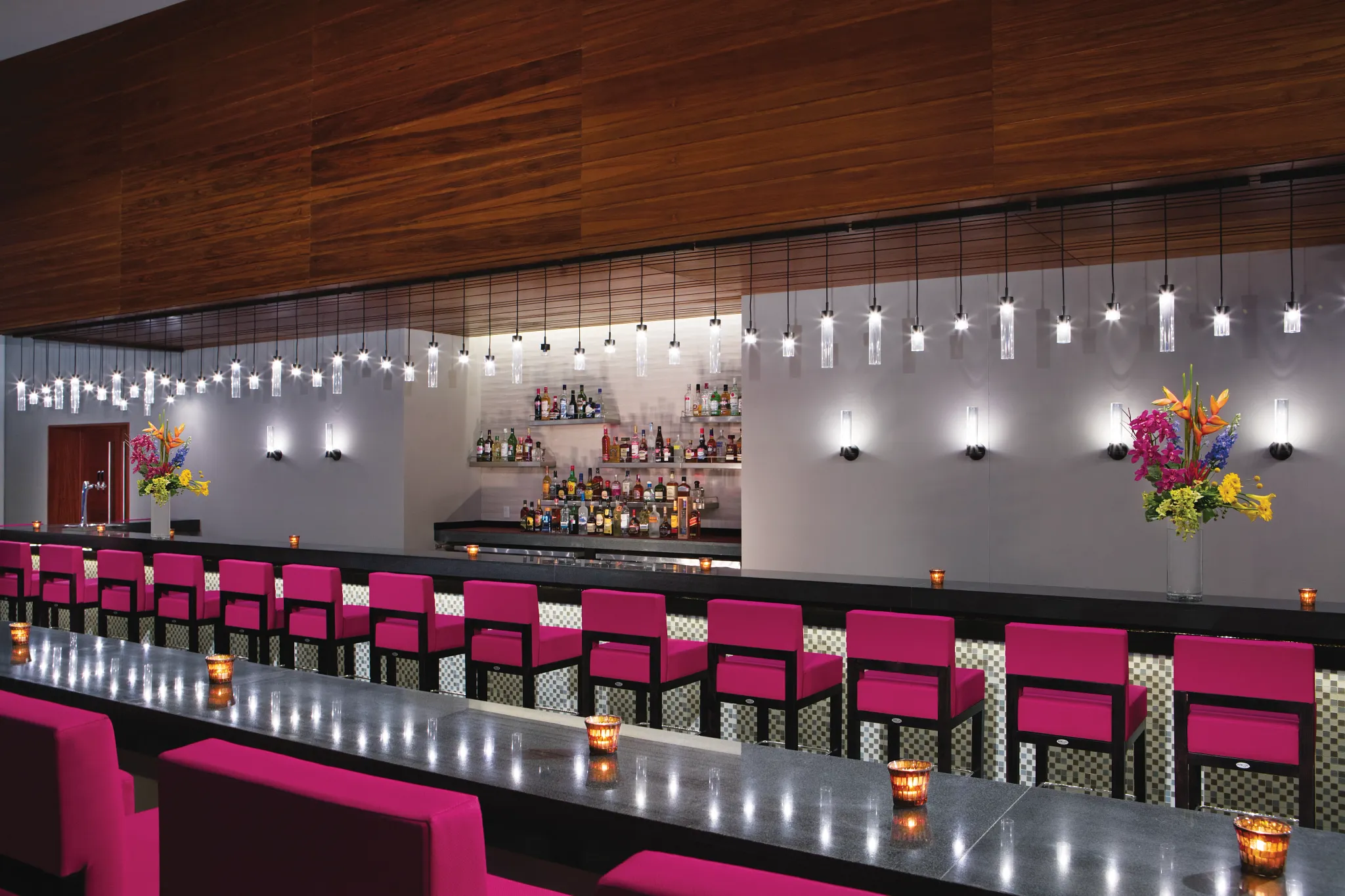 Modern bar interior with pink seating and hanging lights at the Showstopper Bar at Breathless Riviera Cancun.