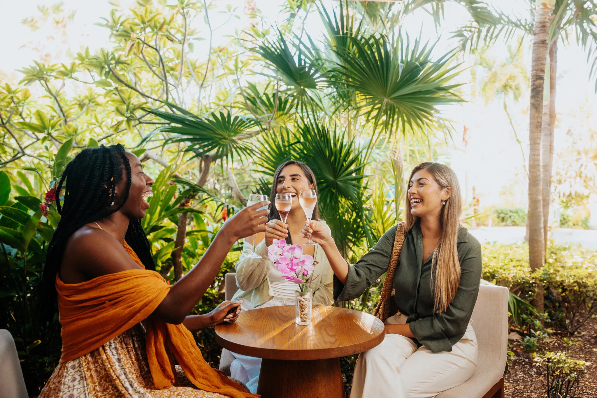 Three women toasting with glasses of sparkling wine among tropical garden surroundings at Breathless Riviera Cancun.
